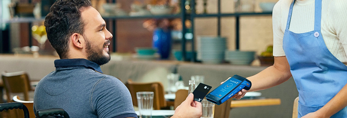 Cliente de restaurante fazendo pagamento com cartão da Caixa na maquininha azulzinha para atendente.